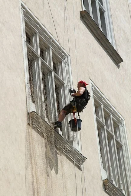 Three window cleaners suspended on ropes clean a modern glass building facade during the day.